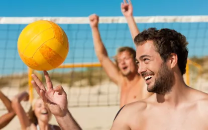 Eine Gruppe von Freunden spielt Beachvolleyball während ihres Kururlaubs am Strand.