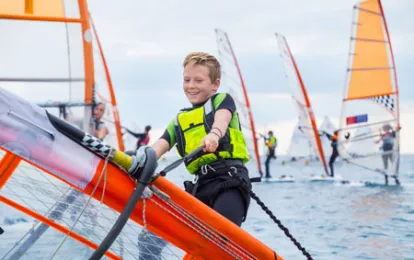 Ein Teenager hebt das Windsurfsegel im Meer auf.