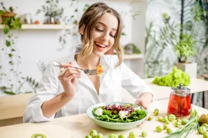 Junge Frau isst gesundes Essen bei Ableitungsdiät in einem schönen Innenraum mit grünen Blumen im Hintergrund