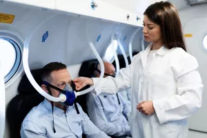 Junge weibliche Ärztin überprüft Maske eines Patienten während einer hyperbären Sauerstofftherapie in dem Kururlaub.