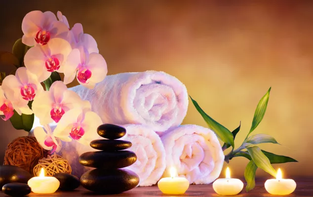 Entspannen Sie bei einer Massage mit warmen Massagesteinen, umhüllt von Handtüchern und Kerzenschein auf einem Naturhintergrund.